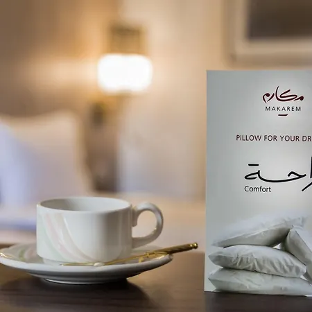 Makarem Ajyad Makkah Hotel Mecca Exterior photo The image features a cozy setting, likely a hotel room. In the foreground, there is a white cup of coffee or tea placed on a small saucer, accompanied by a gold spoon. Beside the cup is a decorative card or sign that reads 